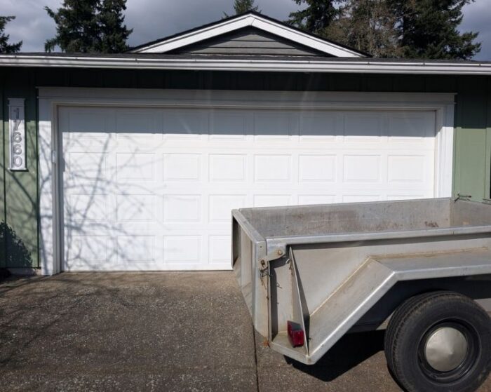 Green home with a white garage door receives an emergency garage door service performed by All About Garage Doors